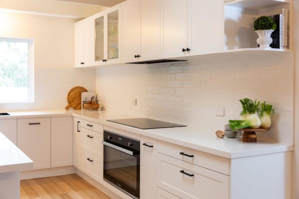 White shaker style kitchen veaturing black handles , oven and cooktop and glass shelves