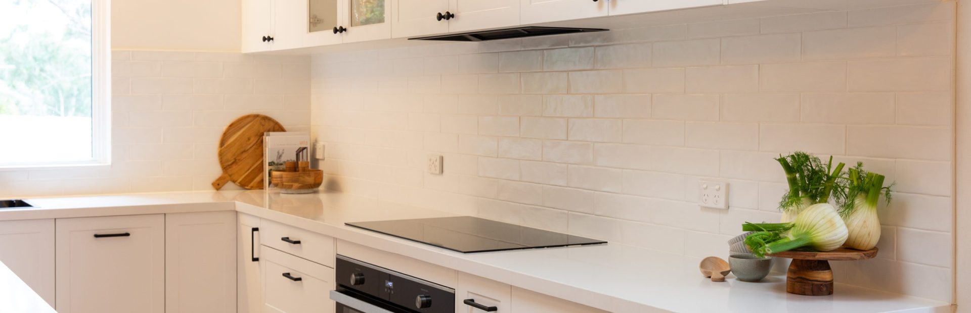 White shaker style kitchen veaturing black handles , oven and cooktop and glass shelves
