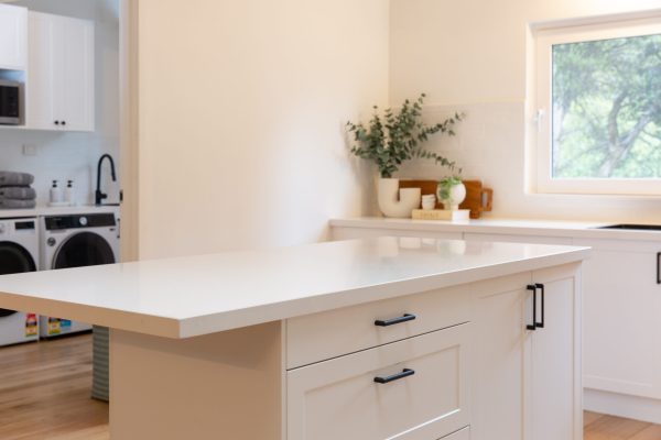 Shaker style white kitchen with central island bench featuring black handles and vases and cooking book styling