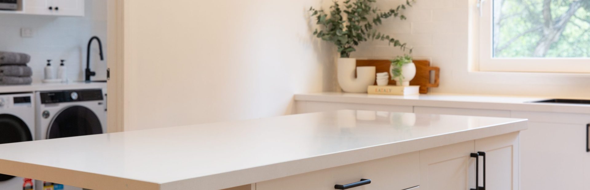 Shaker style white kitchen with central island bench featuring black handles and vases and cooking book styling