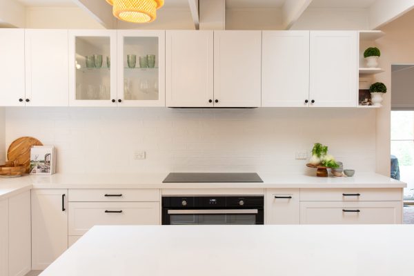 Shaker style white kitchen with black handles and knobs and glass cabinets displaying green glasses and wine glasses