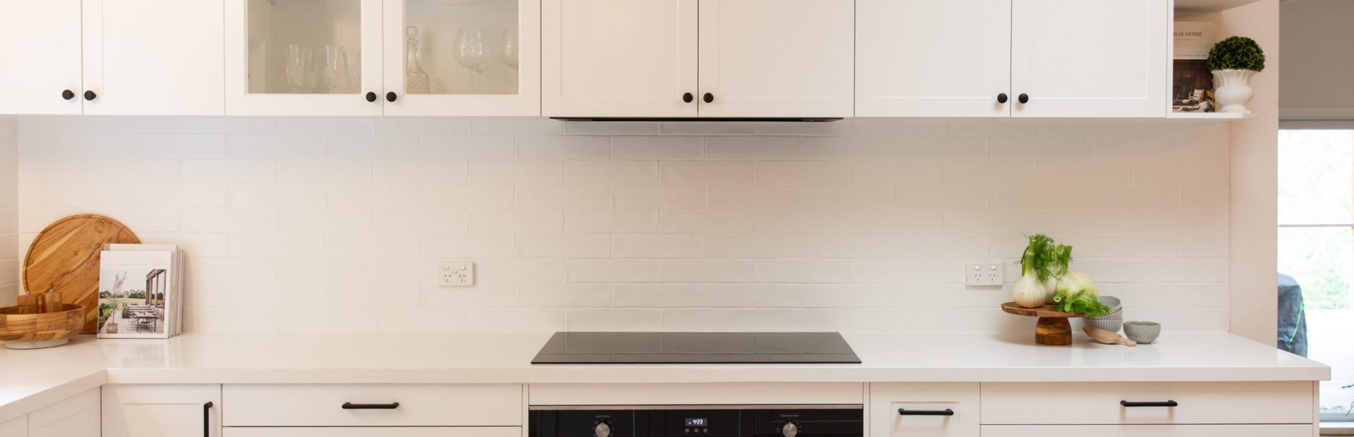 Shaker style white kitchen with black handles and knobs and glass cabinets displaying green glasses and wine glasses