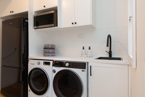 White shaker laundry cabinetry in galley shape with microwave cabinet and pile of grey towels with side by side washer and dryer