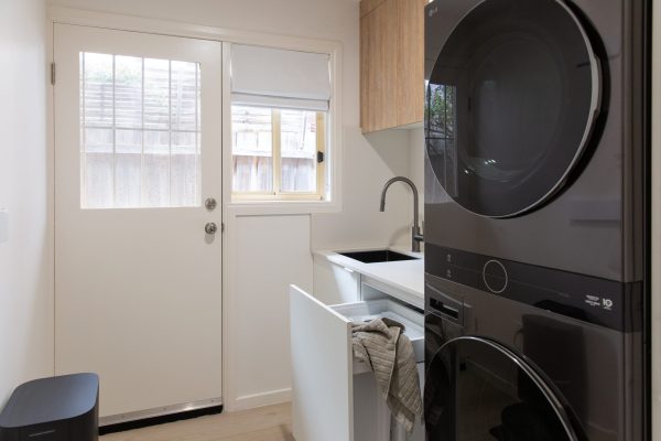 Galley style kitchen featuring black washer dryer and white cabinetry with built in laundry hamper leading with door leading to outside