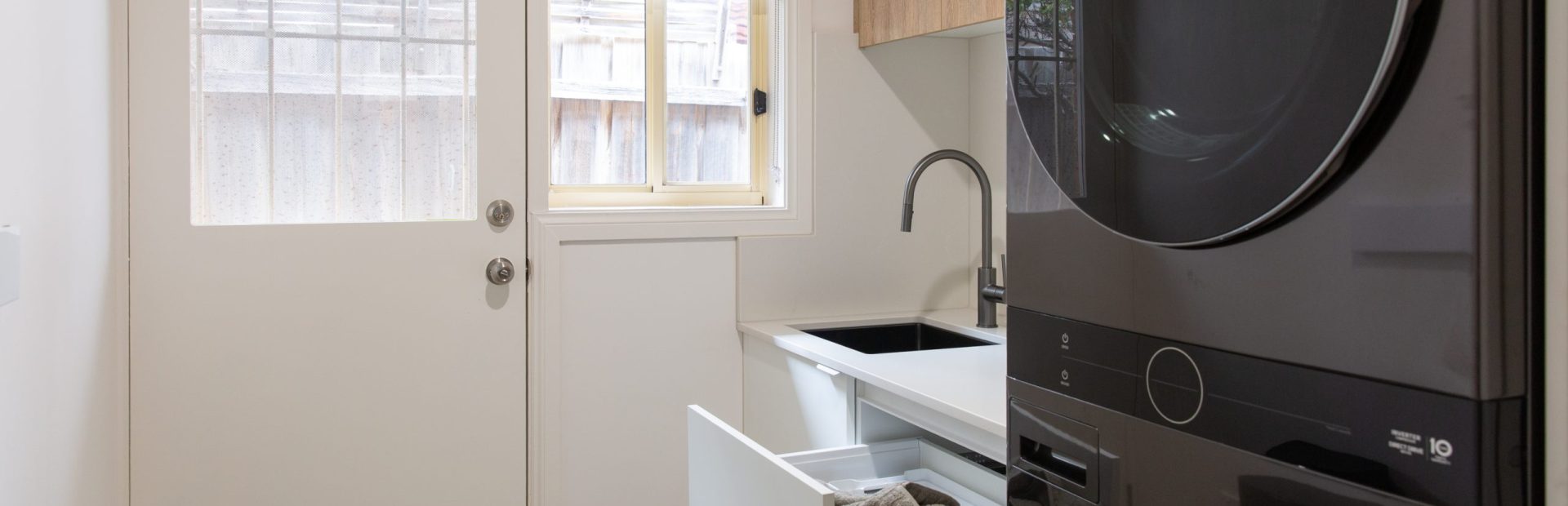 Galley style kitchen featuring black washer dryer and white cabinetry with built in laundry hamper leading with door leading to outside