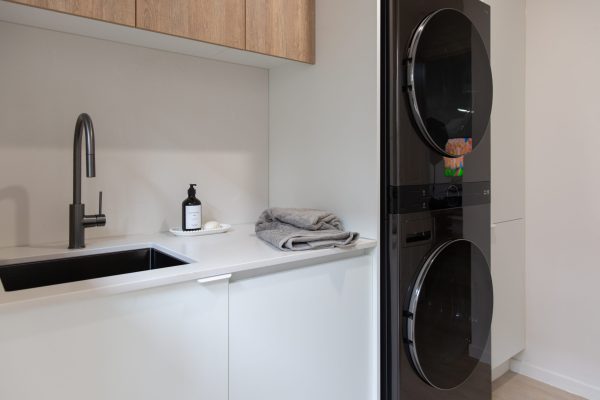White laundry cabinetry with timber laminate overheads in this galley kitchen containing washer dryer in black