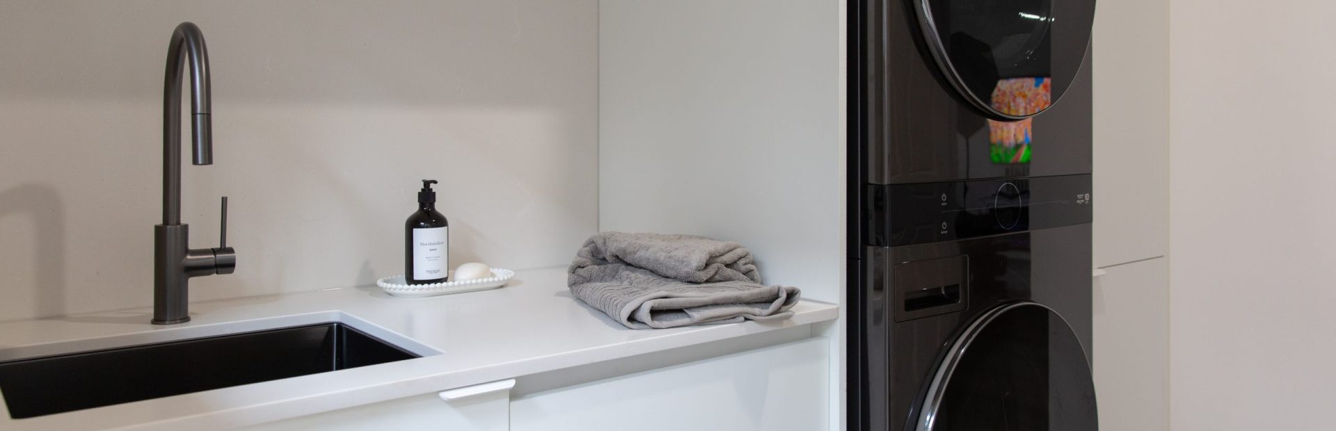 White laundry cabinetry with timber laminate overheads in this galley kitchen containing washer dryer in black