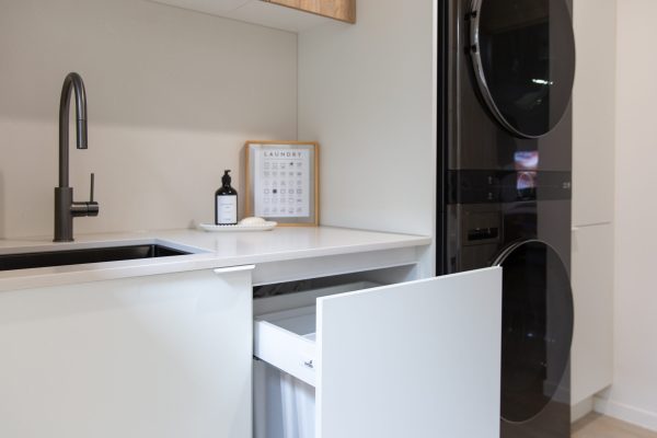 Galley laundry displaying white cabinet containing laundry hamper and double stacked black washer dryer combination