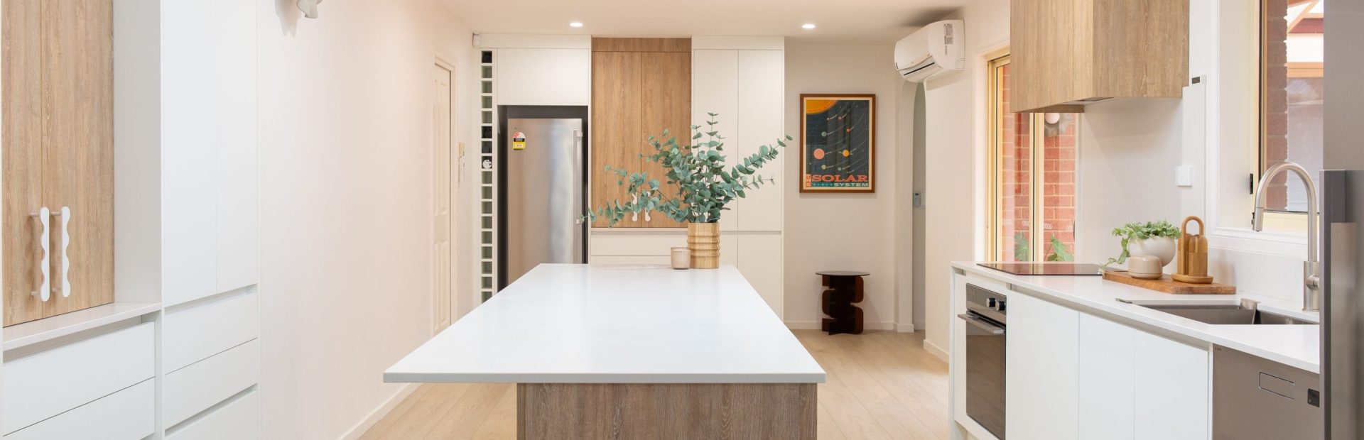 Galley style kitchen featuring large island bench in oak timber with white benchtops displaying overhang for easy seating
