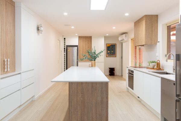 Galley style kitchen featuring large island bench in oak timber with white benchtops displaying overhang for easy seating