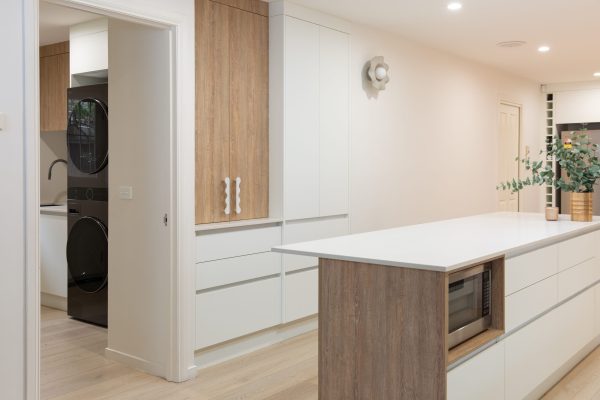 White and oak coloured timber kitchen featuring handle free cabinetry and island bench featuring microwave cabinet