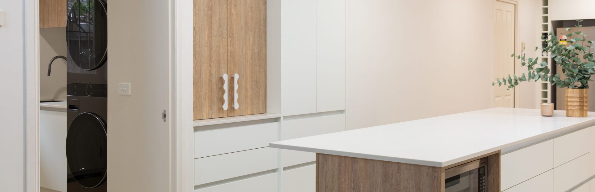 White and oak coloured timber kitchen featuring handle free cabinetry and island bench featuring microwave cabinet