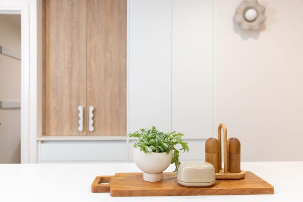 Kitchen displaying oak style appliance cabinet and timber chopping board featuring Country Road Butter and salt and pepper homewares