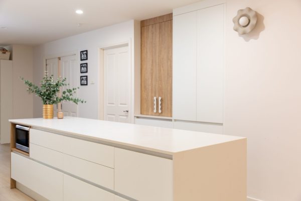 Galley kitchen featuring a bank of white handle free cabinetry with white benchtops and oak style appliance cabinet