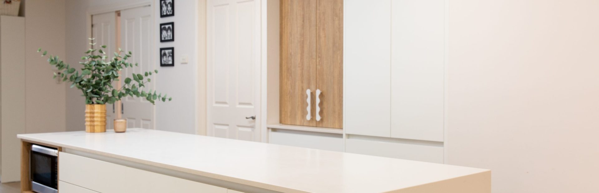 Galley kitchen featuring a bank of white handle free cabinetry with white benchtops and oak style appliance cabinet