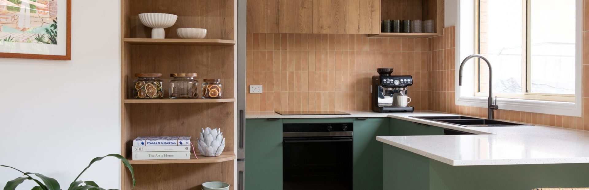 U shaped kitchen in green cabinetry underbench and oak overhead kitchen cabinetry with an tall open oak shelf displaying kitchen styling items