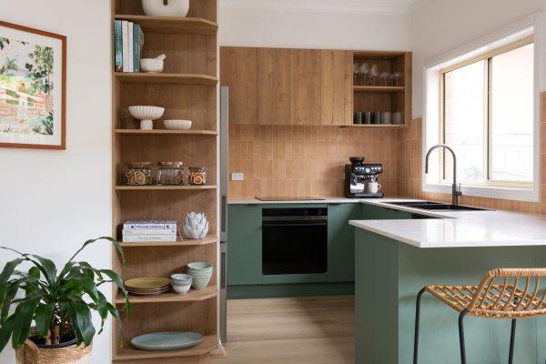 U shaped kitchen in green cabinetry underbench and oak overhead kitchen cabinetry with an tall open oak shelf displaying kitchen styling items