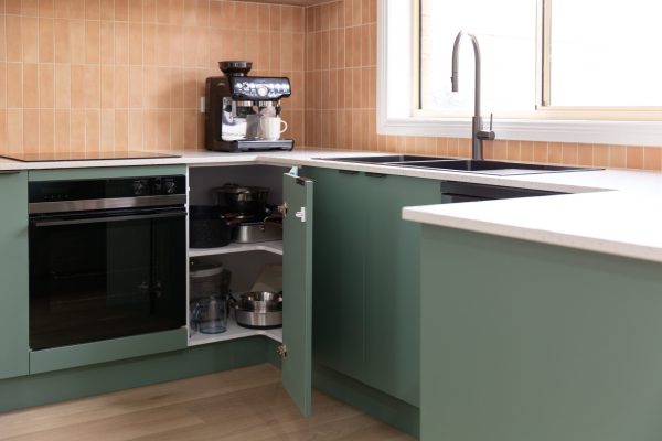 Green kitchen cabinetry featuring corner cabinet with appliances next to a black oven and coffee machine on benchtop