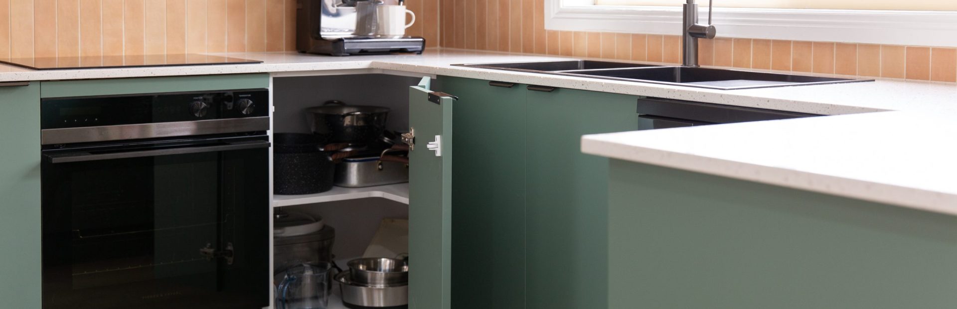 Green kitchen cabinetry featuring corner cabinet with appliances next to a black oven and coffee machine on benchtop