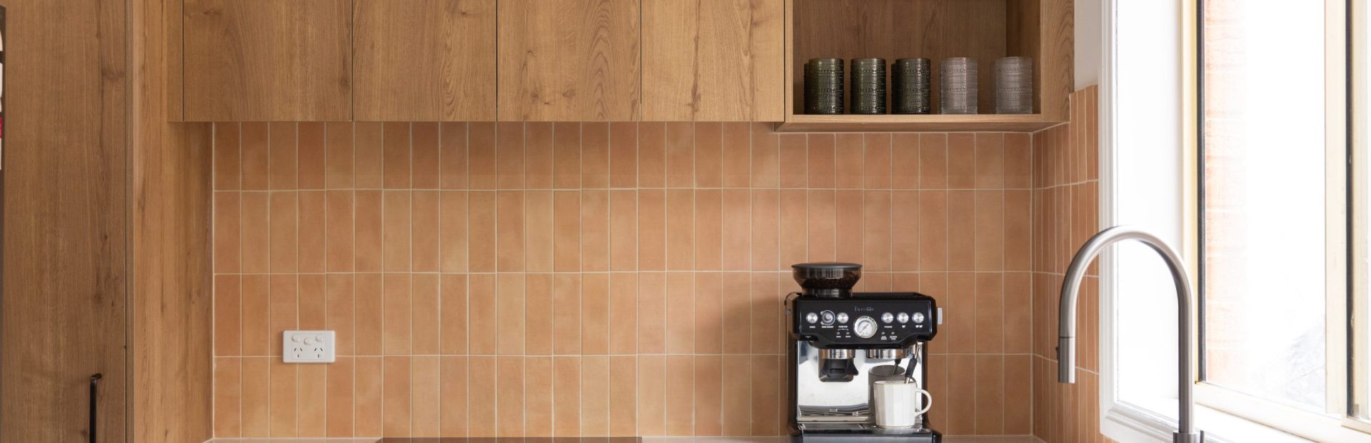 Kitchen featuring timber laminate overhead cabinetry with open shelf displaying glassess and green cabinetry below white stone benchtops