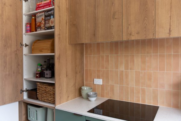 Kitchen pantry featuring oak laminate with pantry staples and white benchtops with green cabinetry
