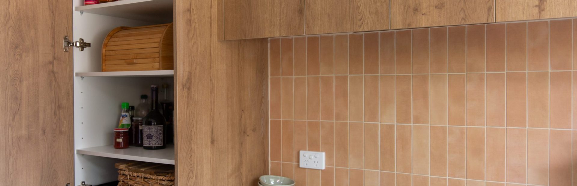 Kitchen pantry featuring oak laminate with pantry staples and white benchtops with green cabinetry