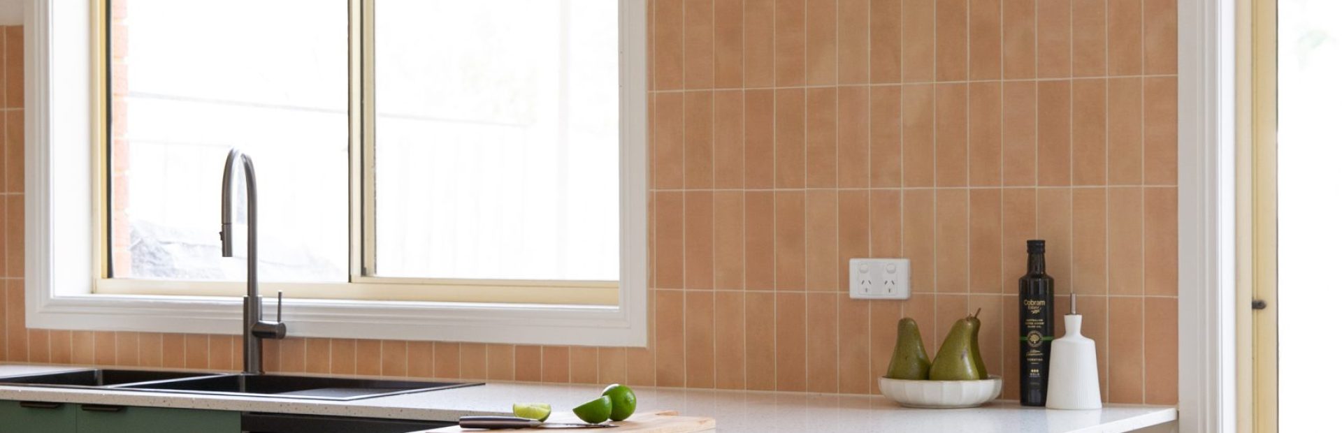 Green kitchen cabinetry with overhang white benchtop with timber and black breakfast bar stools