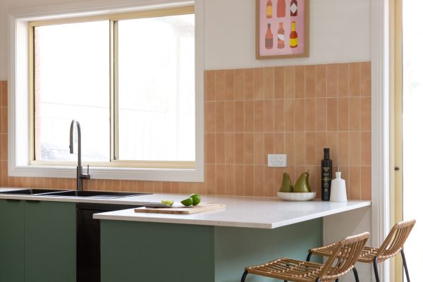 Green kitchen cabinetry with overhang white benchtop with timber and black breakfast bar stools