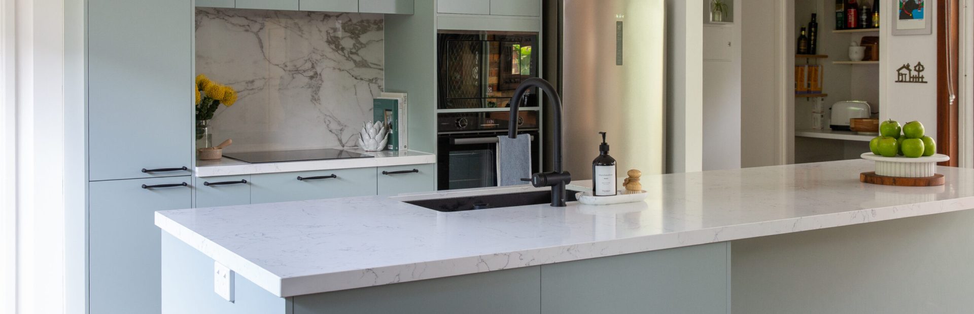 Green and white galley kitchen featuring large island bench with additional storage in the front