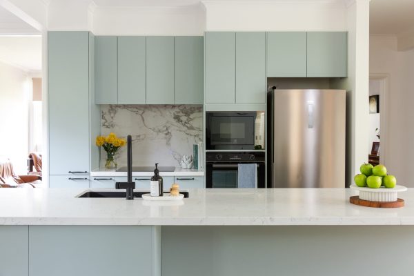 Green kitchen cabinetry featuring white stone benchtop and marble stone splashback