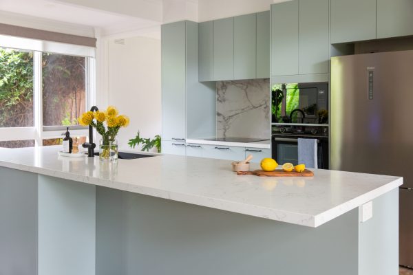 Light green galley kitchen displaying large island bench with stone waterfall island for bench seating