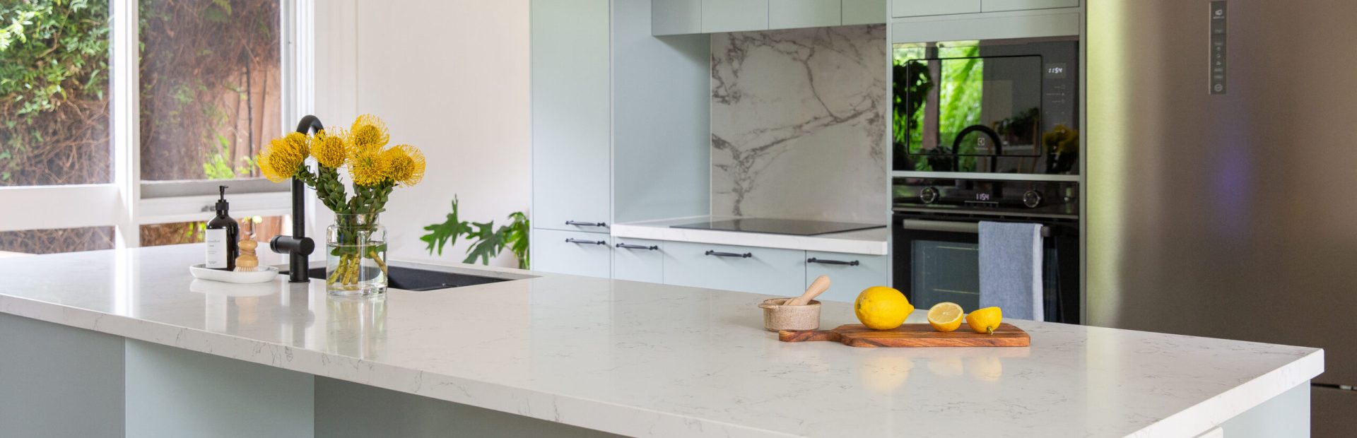 Light green galley kitchen displaying large island bench with stone waterfall island for bench seating