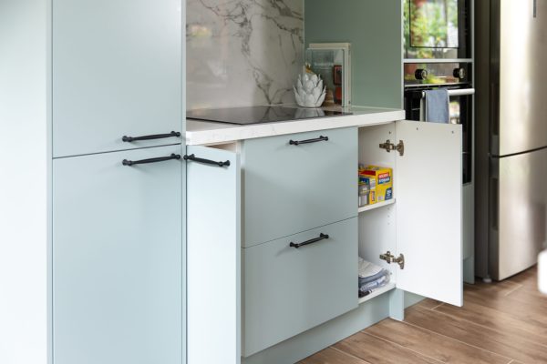 Light green colour cabinetry displaying a variety of cupboards with pantry items and cooktop above