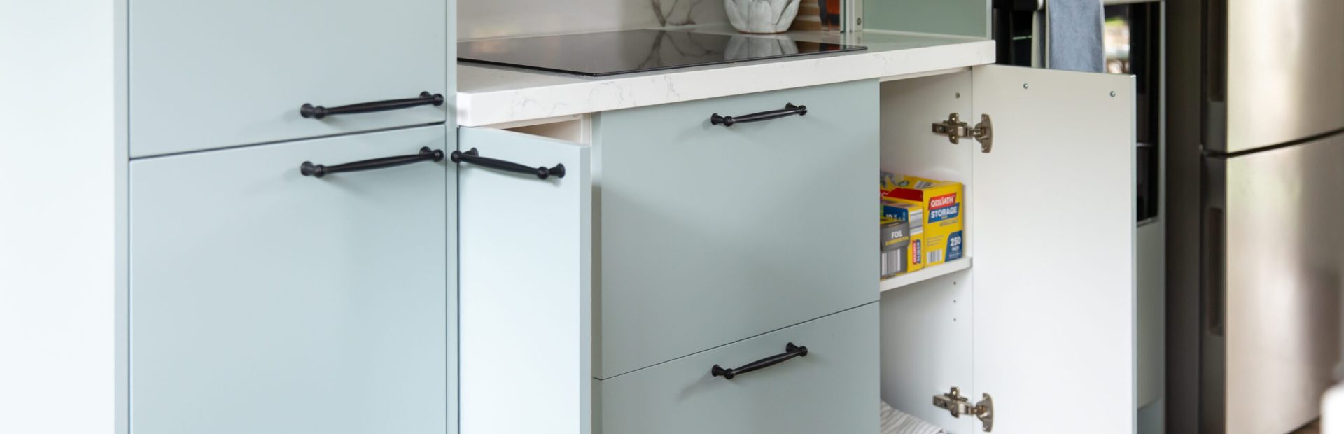 Light green colour cabinetry displaying a variety of cupboards with pantry items and cooktop above