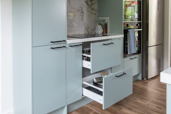 Green kitchen cabinetry displaying pull out deep drawers with pots and pans