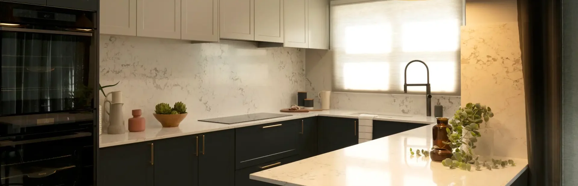 Galley style kitchen featuring shaker cabinetry in terril base and oyster colour overhead cabinetry with pendant lights in brass and white stone benchtops with styling items on bench as featured on Selling Houses Australia in North Fitzroy